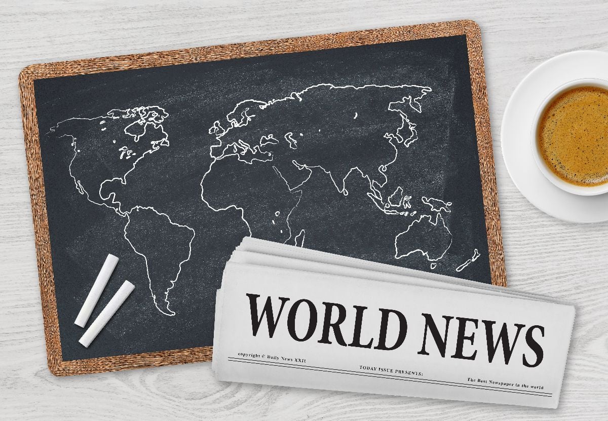 World news, chalkboard map, and coffee on a table.