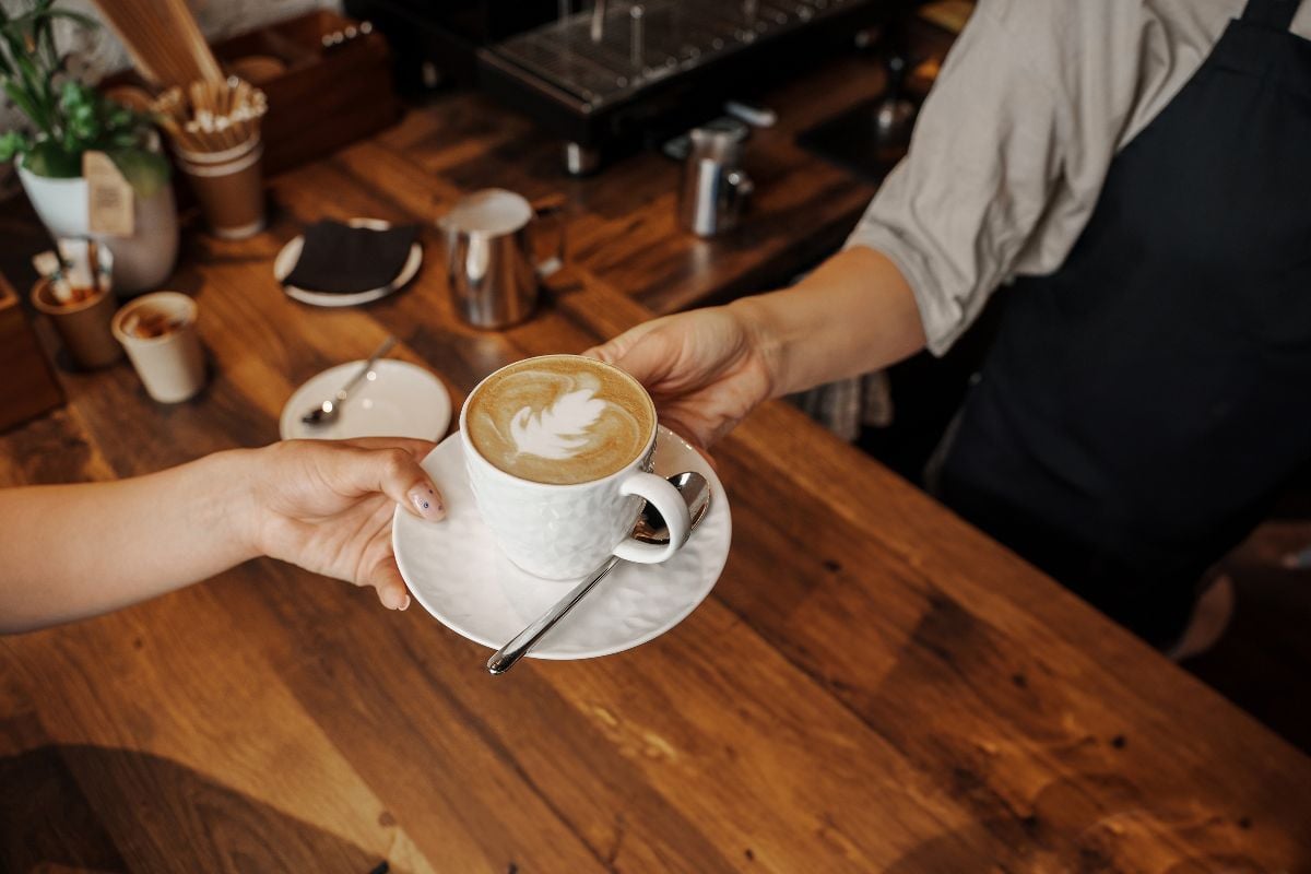 A barista hands over a crafted cappuccino with latte art to a customer.