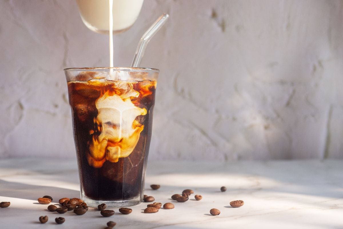 Pouring milk into a glass of homemade iced cold brew coffee.