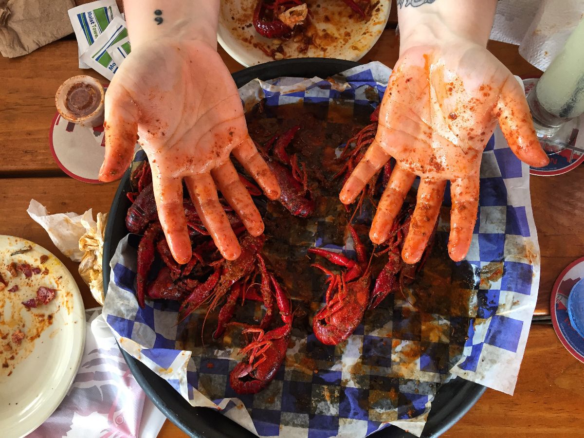 Meal finished and hands stained with crawfish seasoning over basket of crawfish.