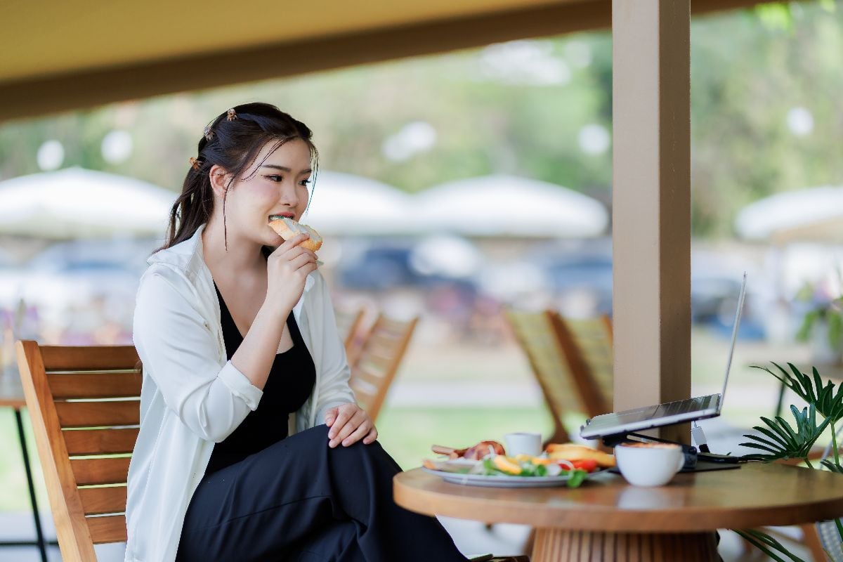 A young woman works while having breakfast at an outdoor café.