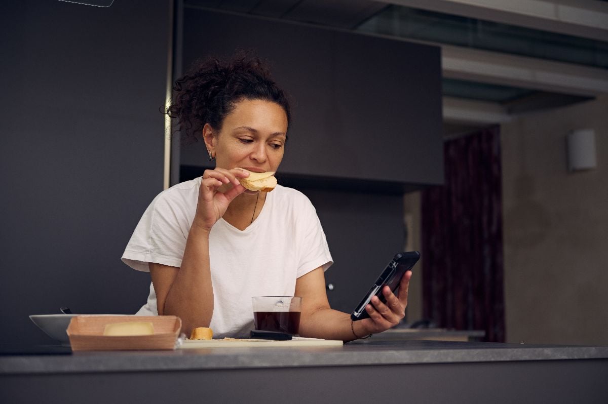 Woman eating sandwich and checking social media.