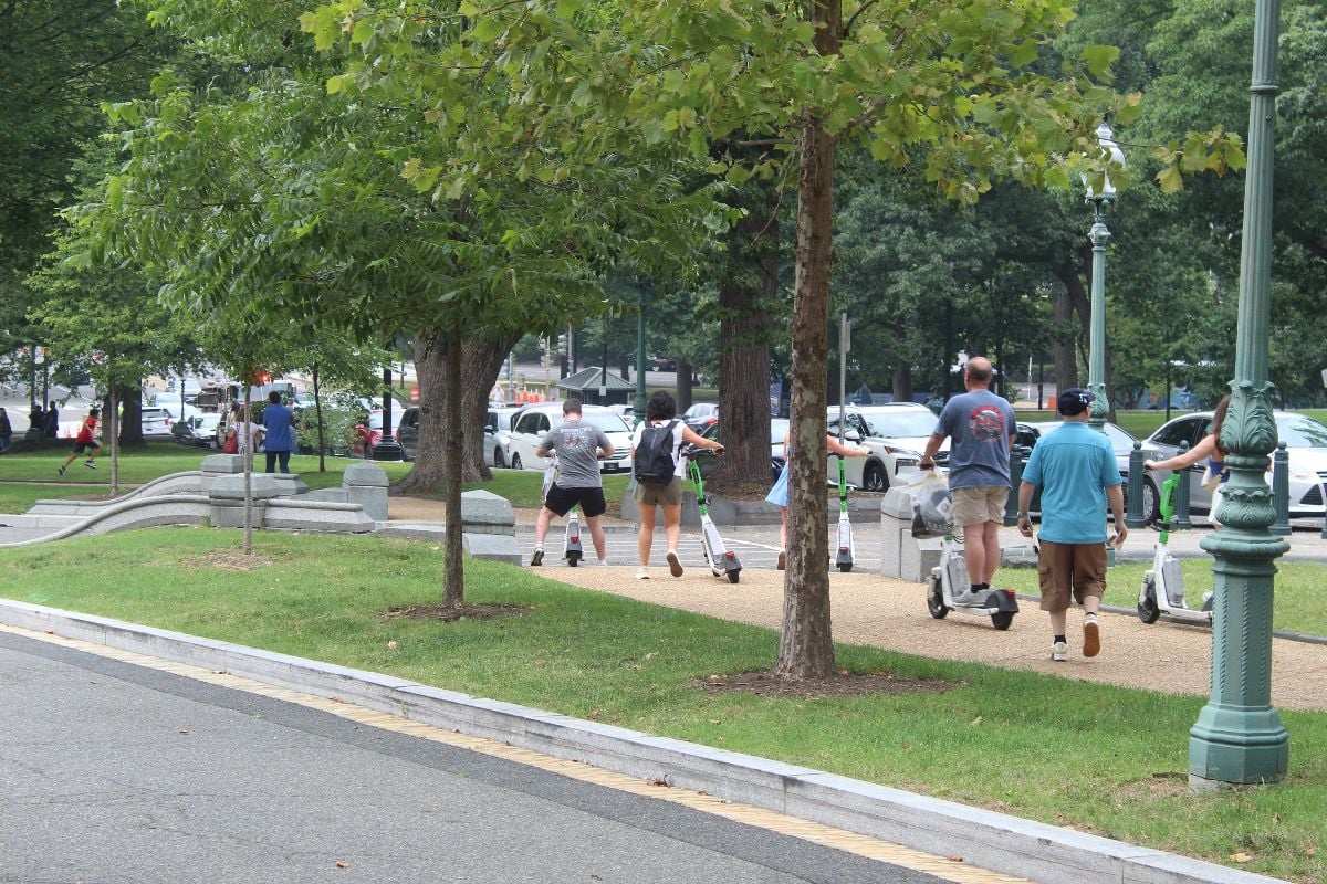 A photo of a group of adults using electric scooters along a path.
