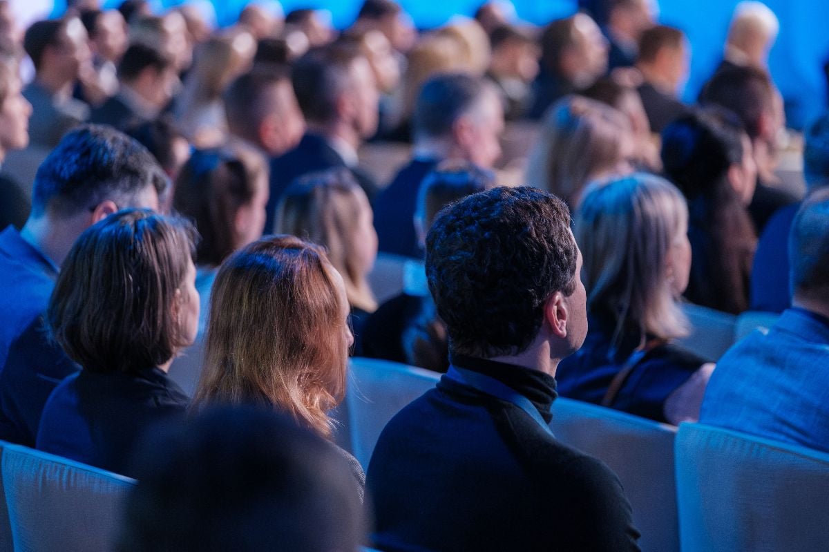 Diverse audience of professionals intently listens to a speaker at a conference event.