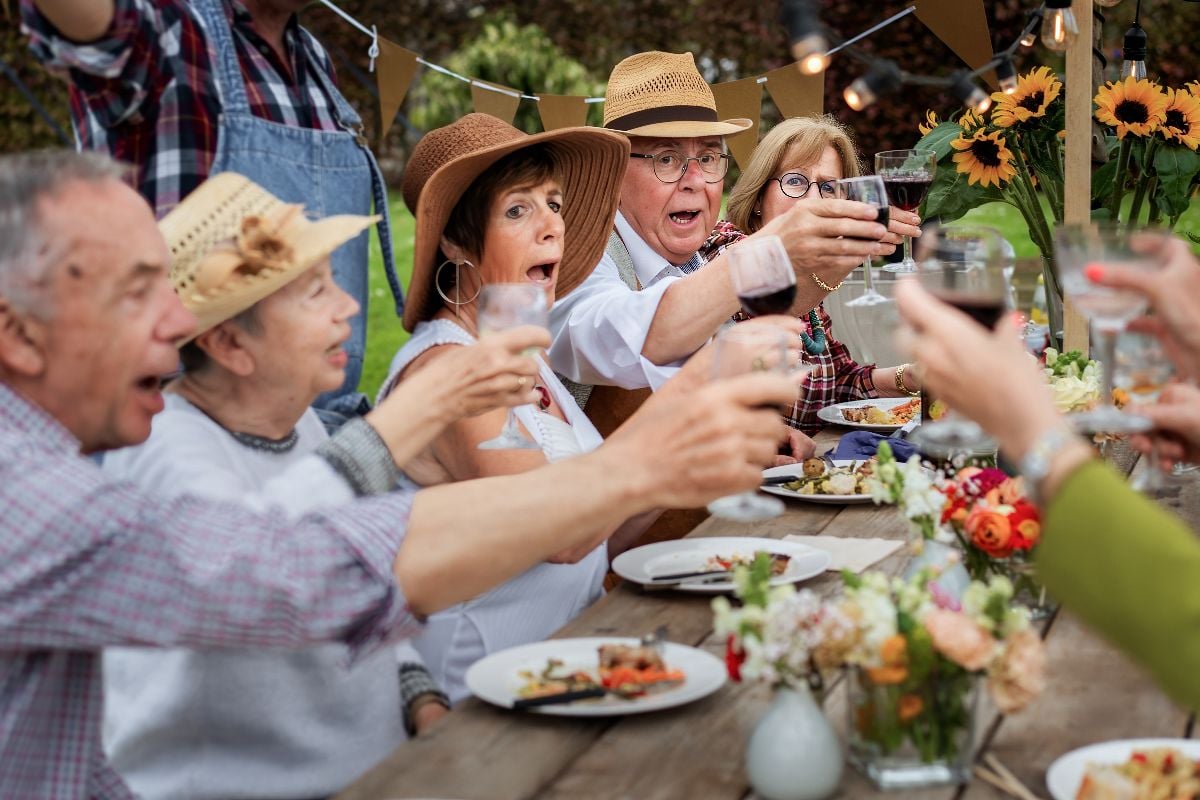 Senior friends raising glasses for a toast at an outdoor garden party.