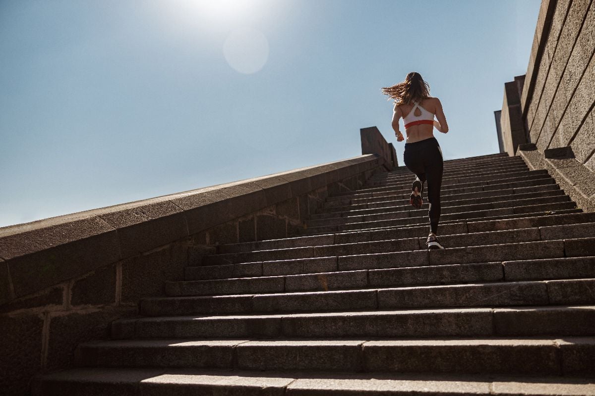 Sportive lady in tracksuit runs up old stone steps under clear sky.