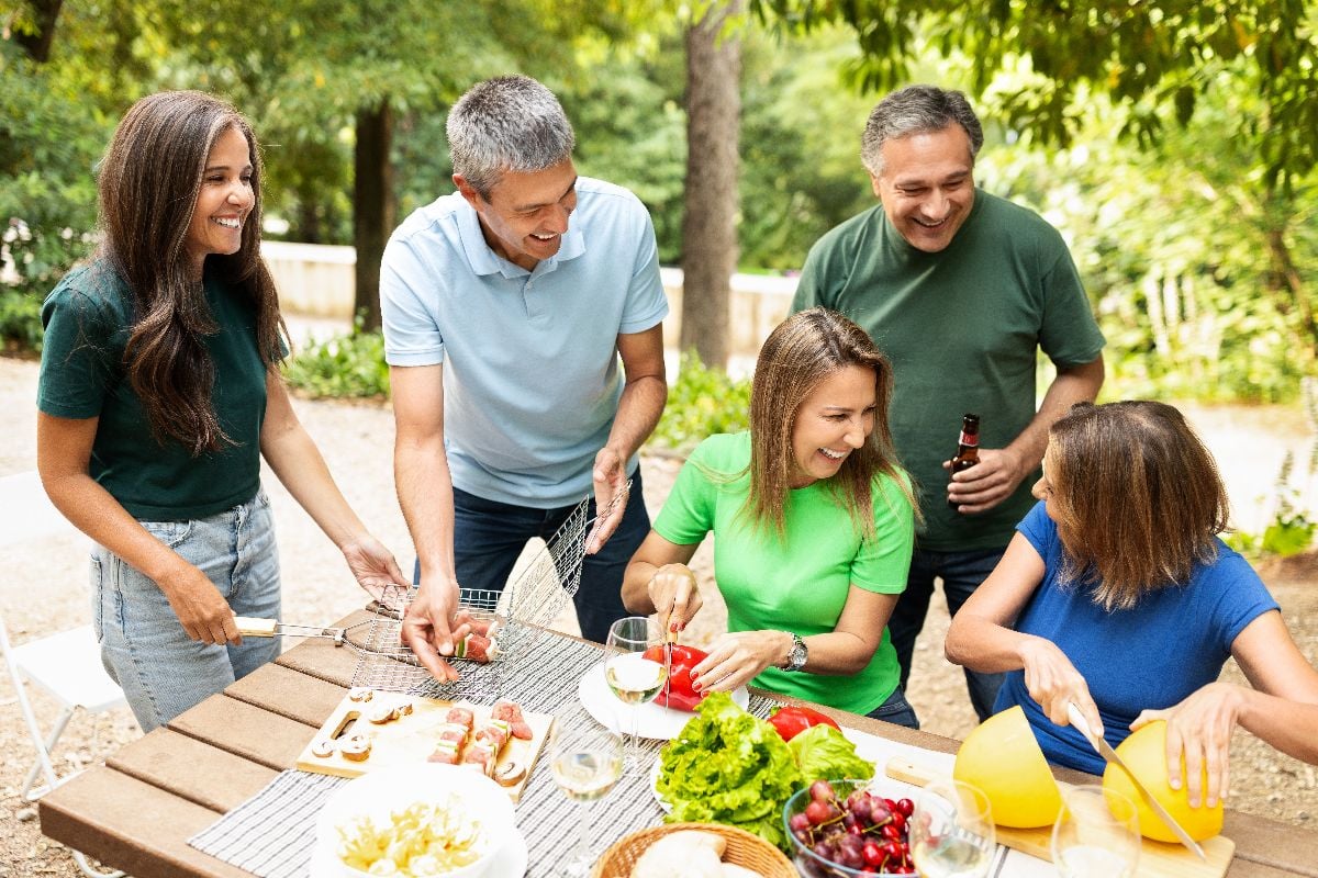 A lively group of friends shares laughter and delicious food while grilling in a green park.