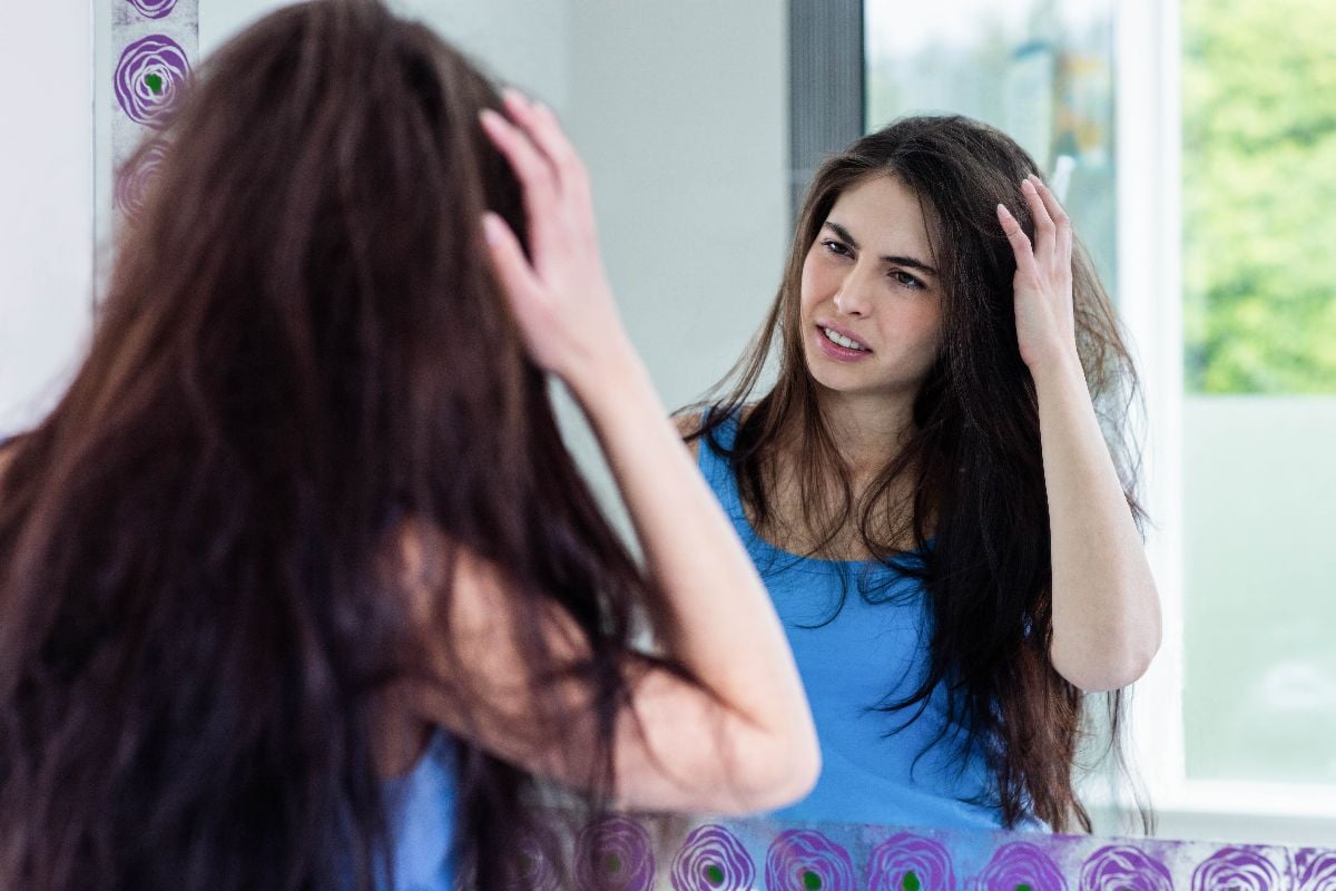 Woman looking at her frizzy hair through a mirror.
