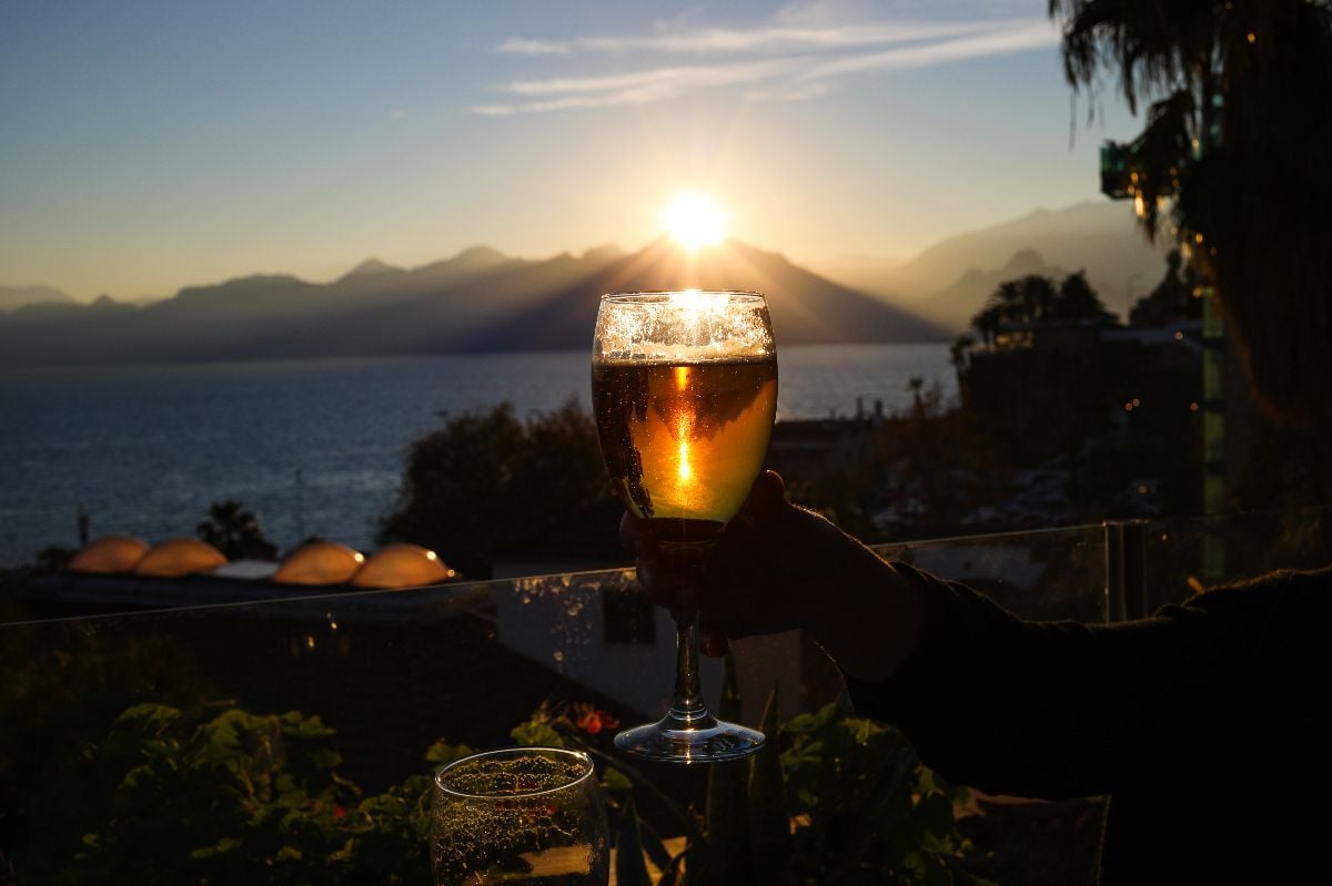 Cheers with two glasses of beer against sunset and mountains.