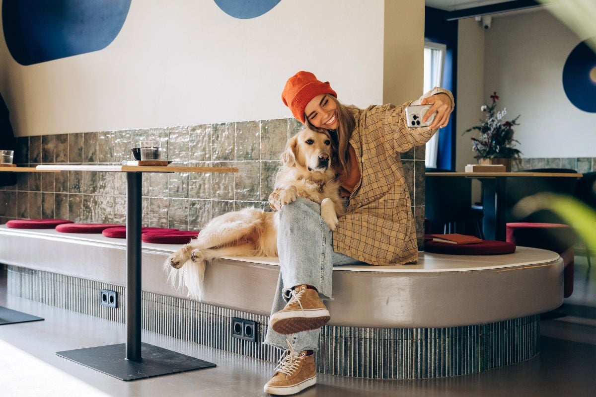 Woman taking a selfie with her golden retriever dog in a cafe.