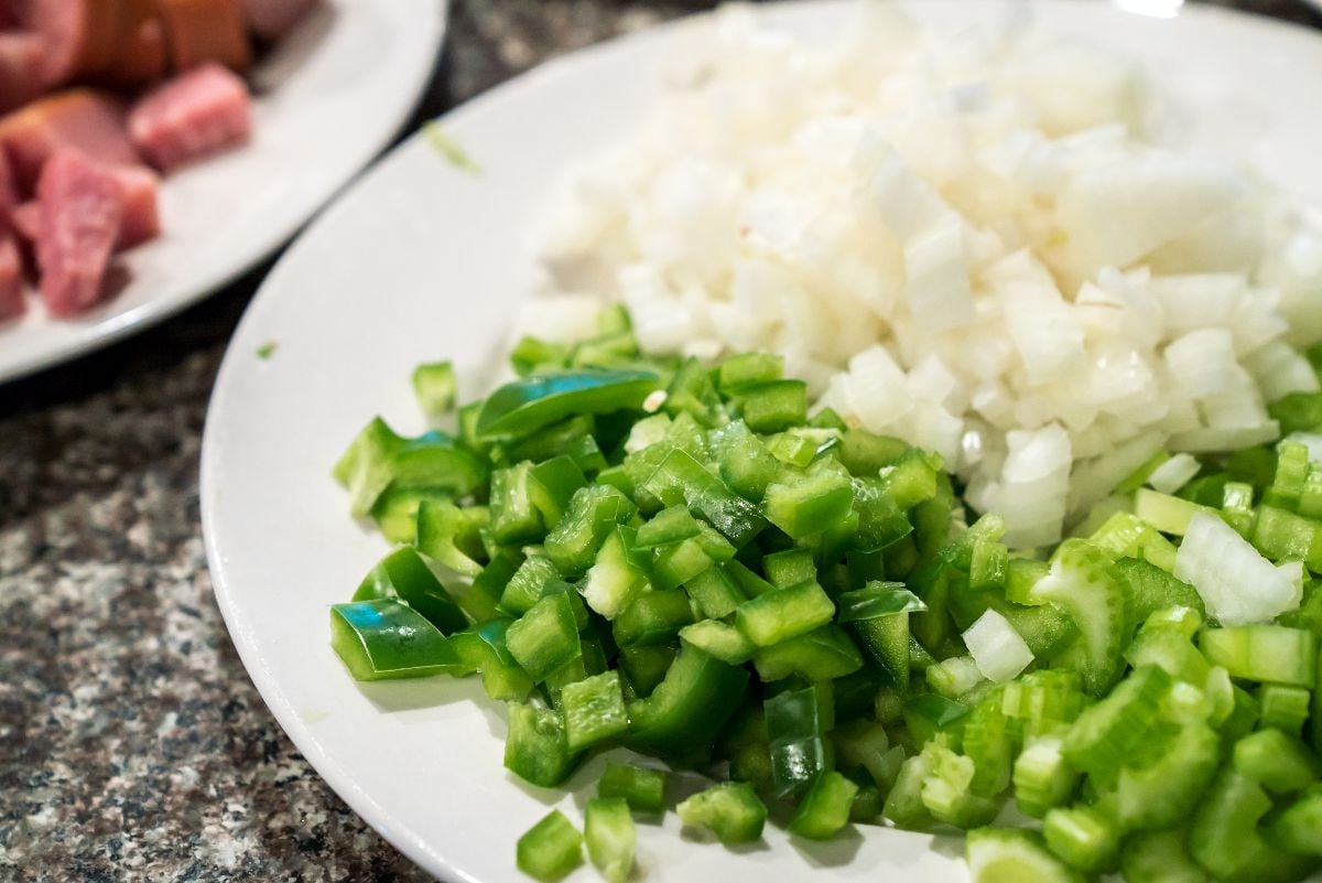 A cajun mirepoix of onion, celery, and green bell pepper, sits diced and prepped on a white plate.