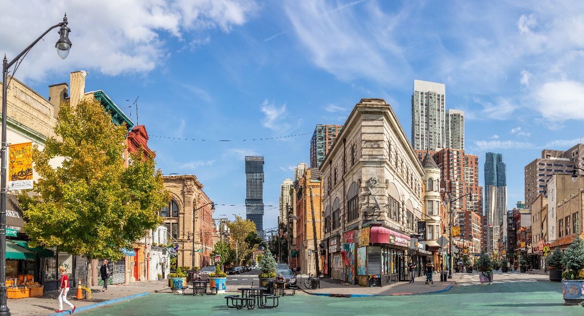 Lively square in downtown Jersey City with historic buildings, modern skyscrapers, street art, and greenery,.