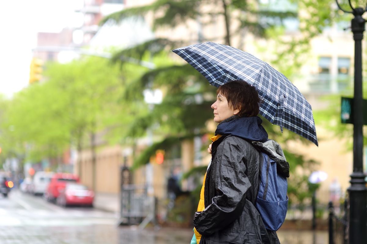 Woman with umbrella walking on street in cool rainy spring day.