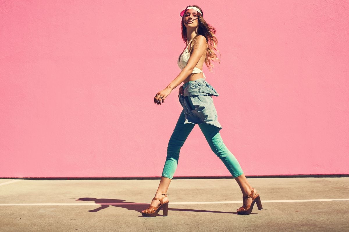 Woman walking against pink wall in jeans shirt and mint pants.