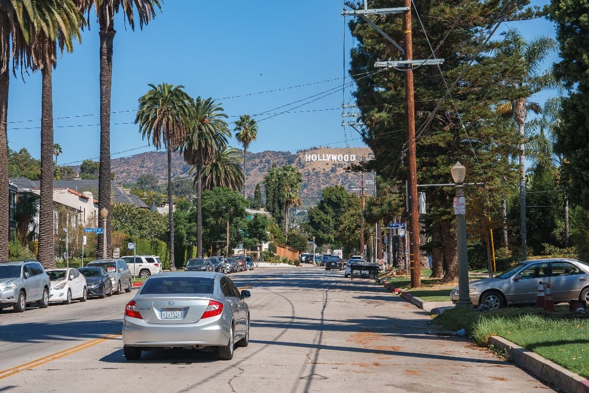 Cars are parked along the sides, with a silver car driving.