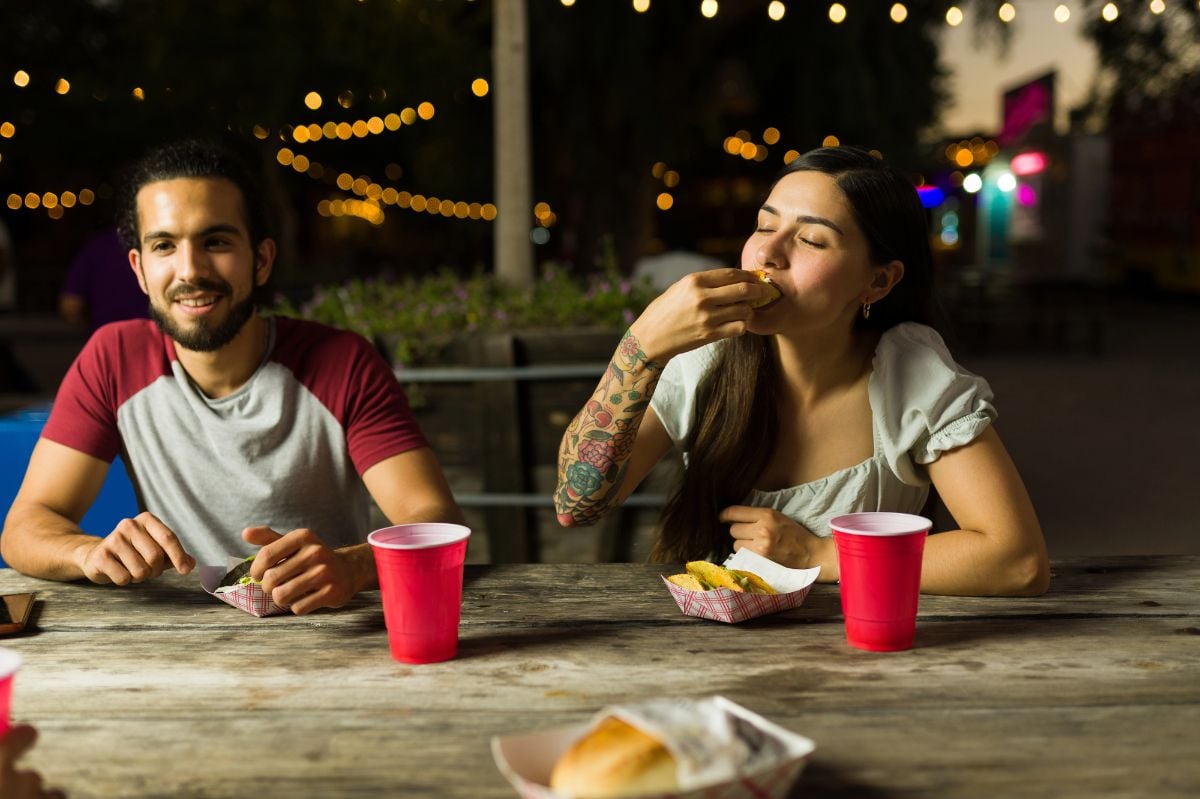Hungry woman and man eating street tacos at night.