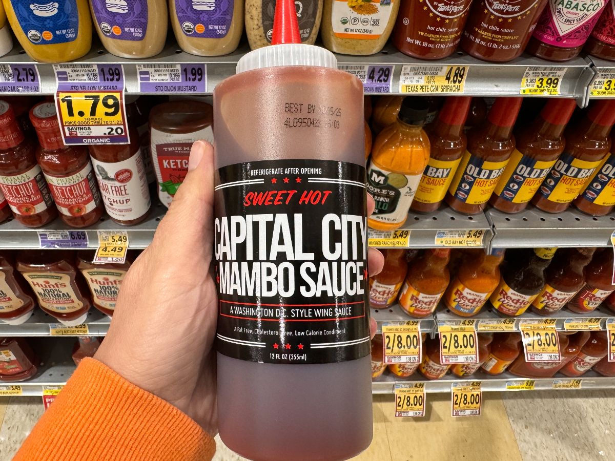 Hand holds up a bottle of Capital City Mambo Sauce for sale at a grocery store.