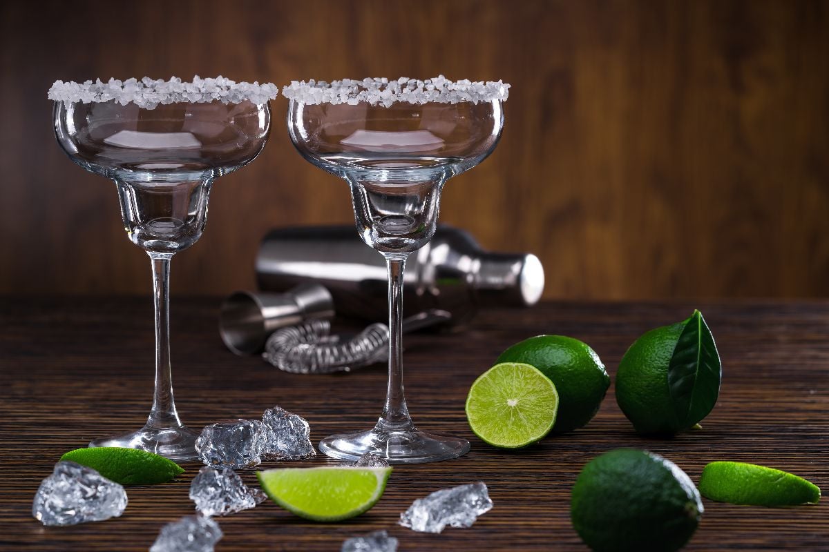 Margarita cocktail on wooden table with ice, limes and schaker.