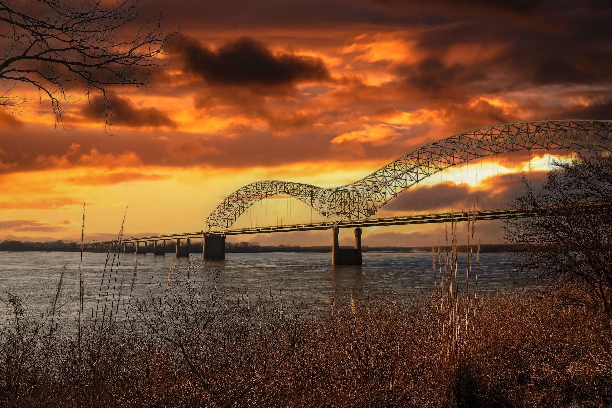 Memphis-Arkansas Bridge over the vast flowing waters of Mississippi river at sunset.