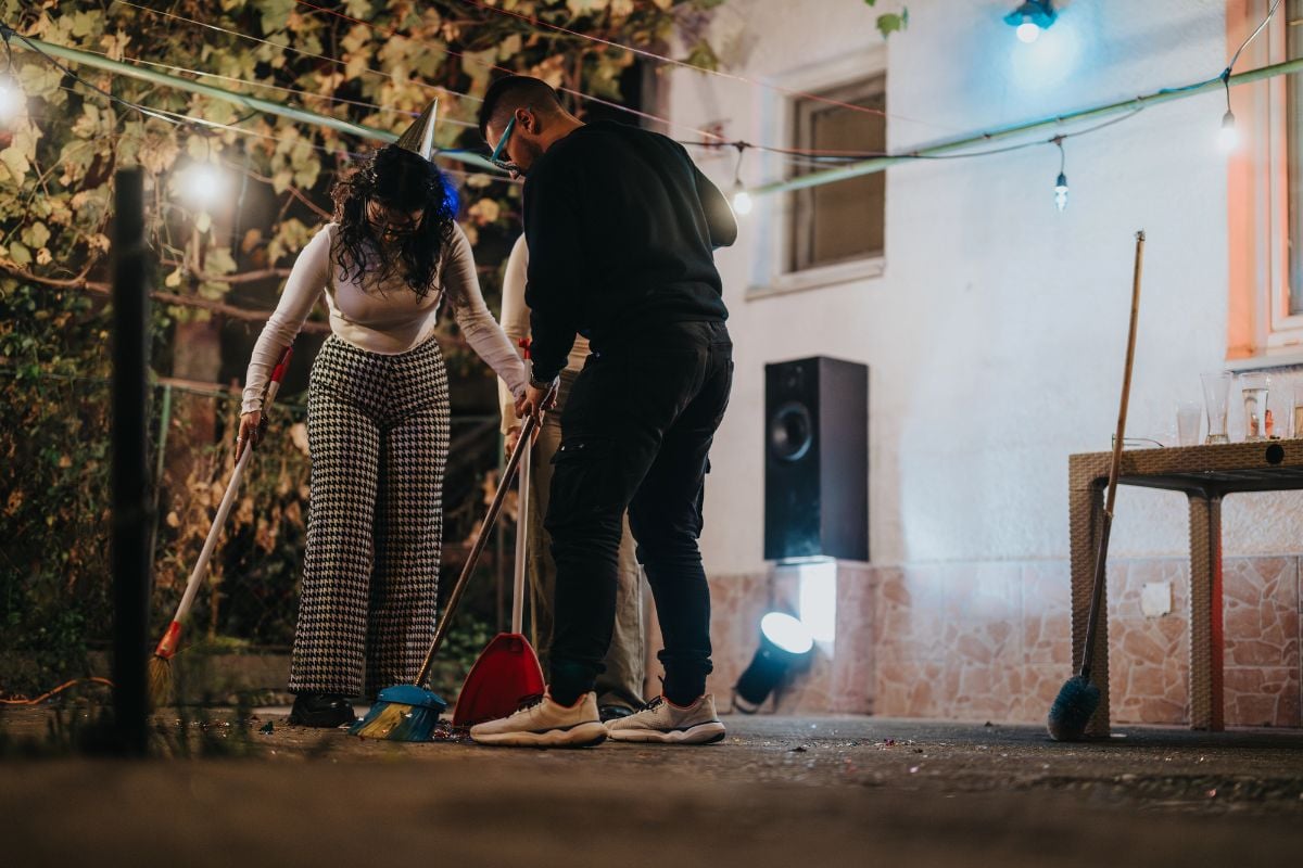 Neighbors sweep confetti and debris under string lights.