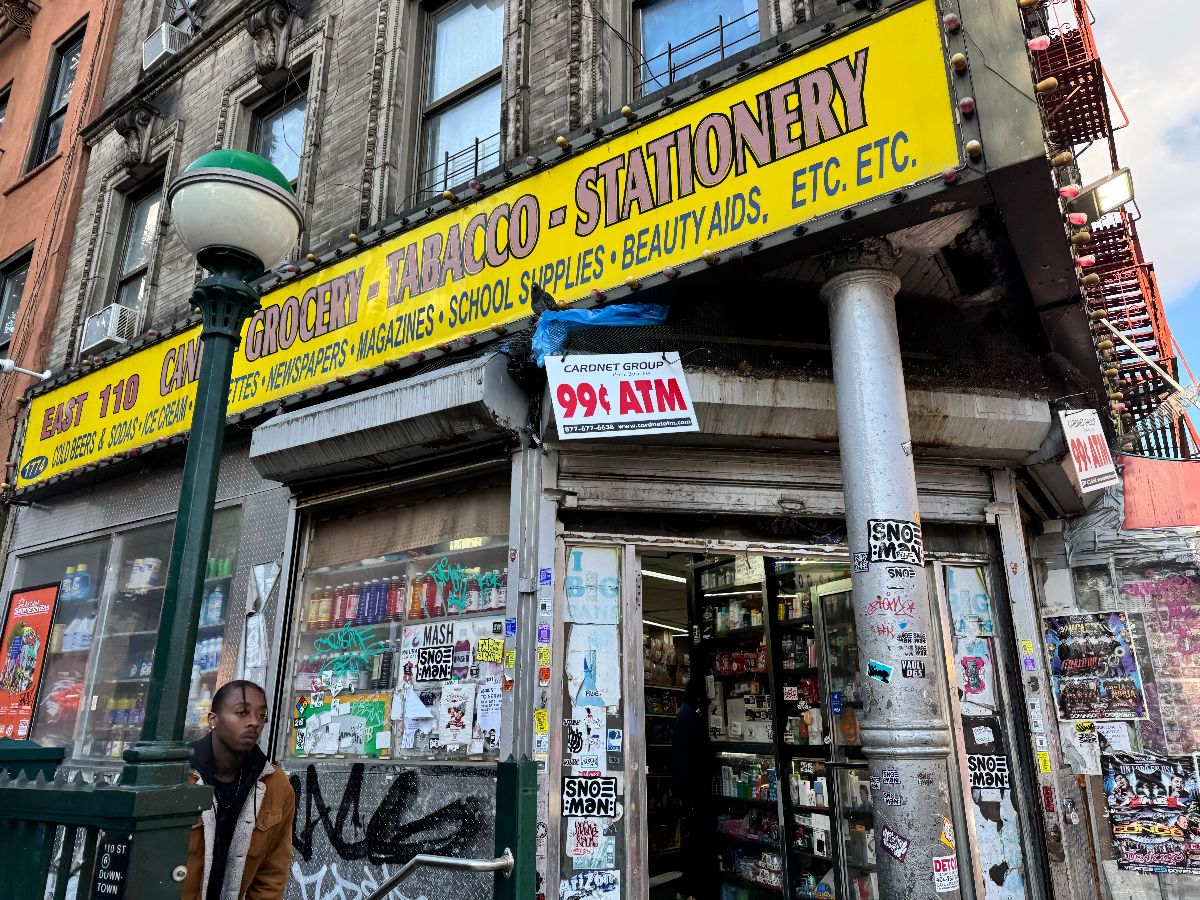 Man exiting subway station in front of a corner bodega in East Harlem, Manhattan.