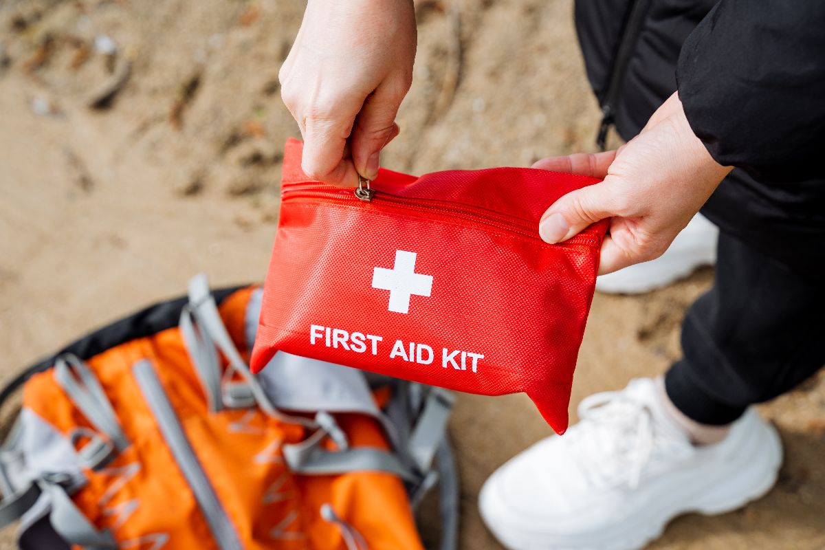 A person attentively packs a first aid kit into a backpack for travel or recreation.
