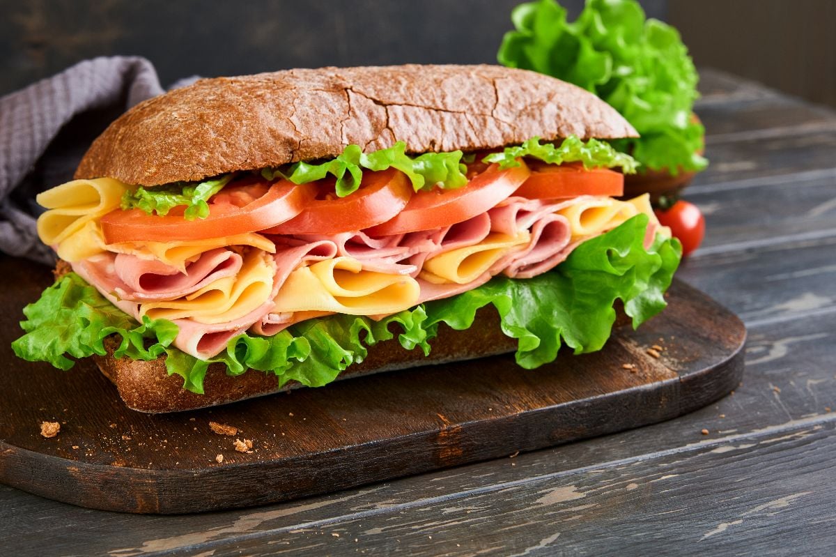 One fresh big submarine sandwich with ham, cheese, lettuce, and tomatoes.