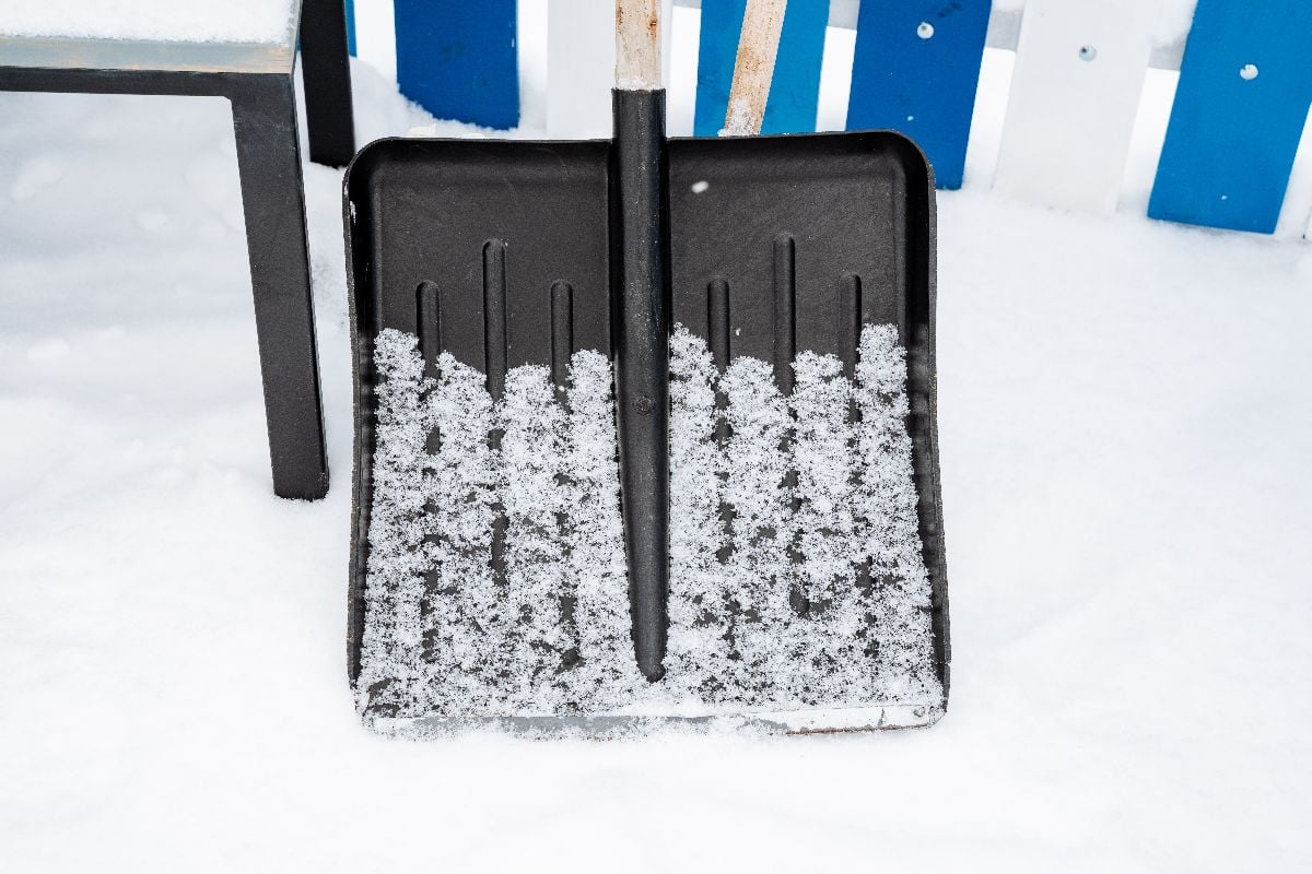 A silver shovel rests in the snow beside a chair.