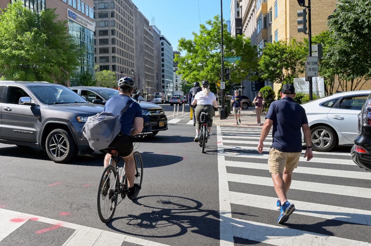 Cyclists and pedestrians between cars across a road junction on their way to work in central Washington DC.