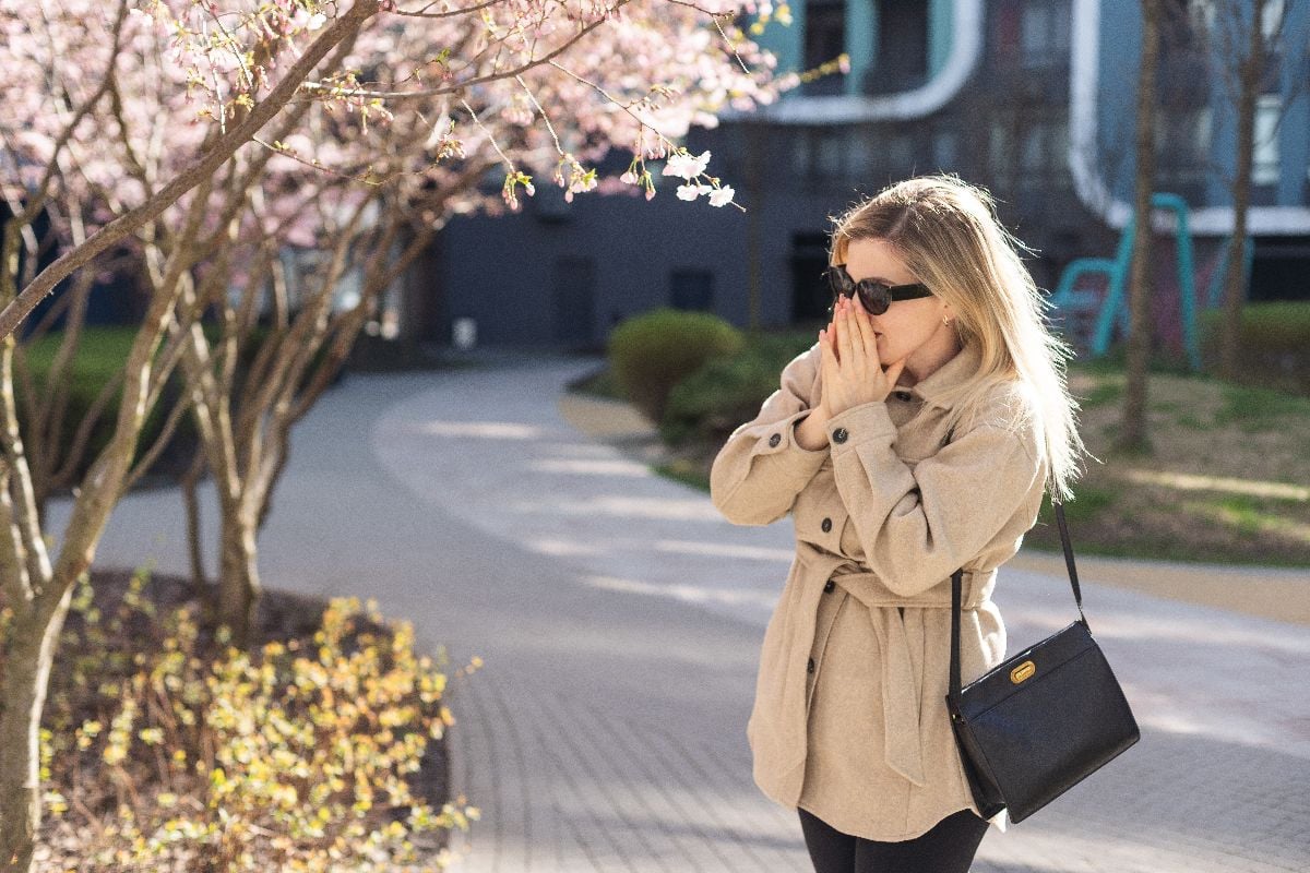 Woman suffering from seasonal allergy at spring in blossoming garden.