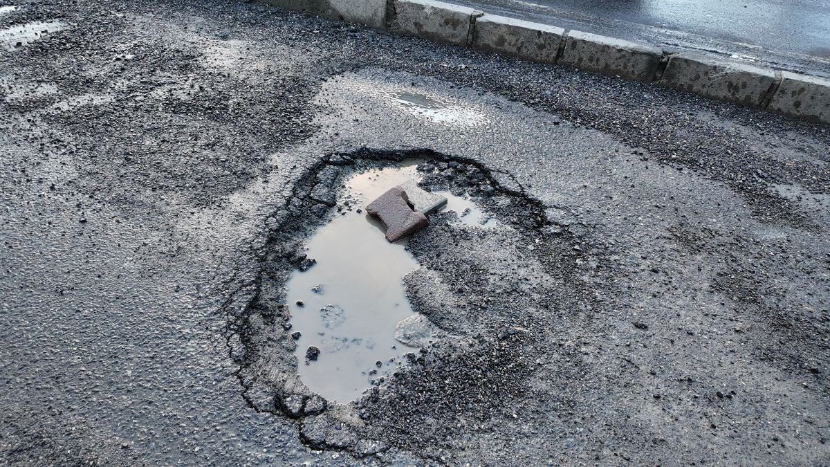 Pothole filled with water and debris on urban road after rainfall.