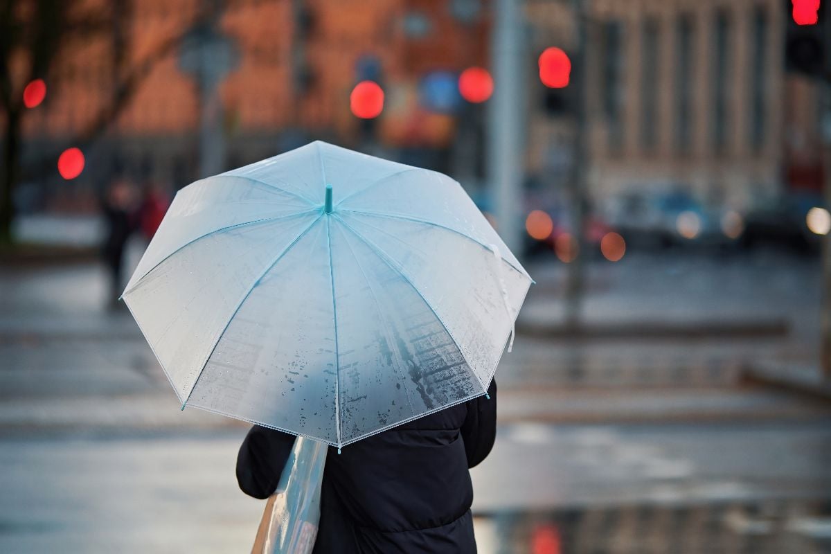 Woman with white umbrella waiting signal for cross walk during rain.