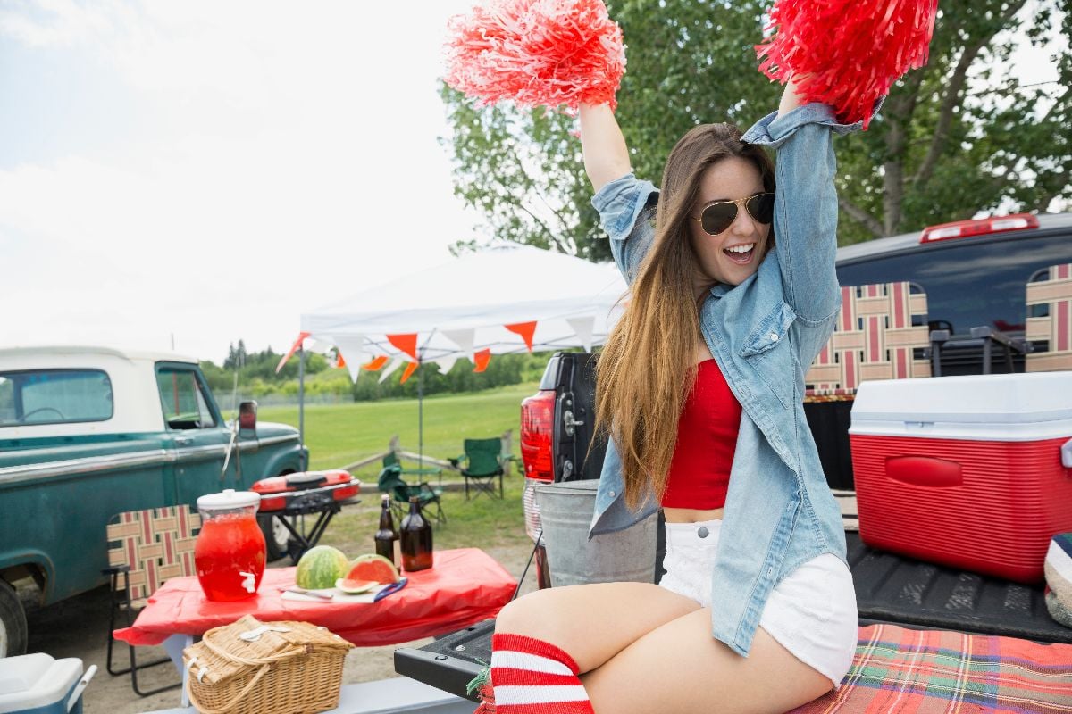 Woman cheering at tailgate barbecue in field.