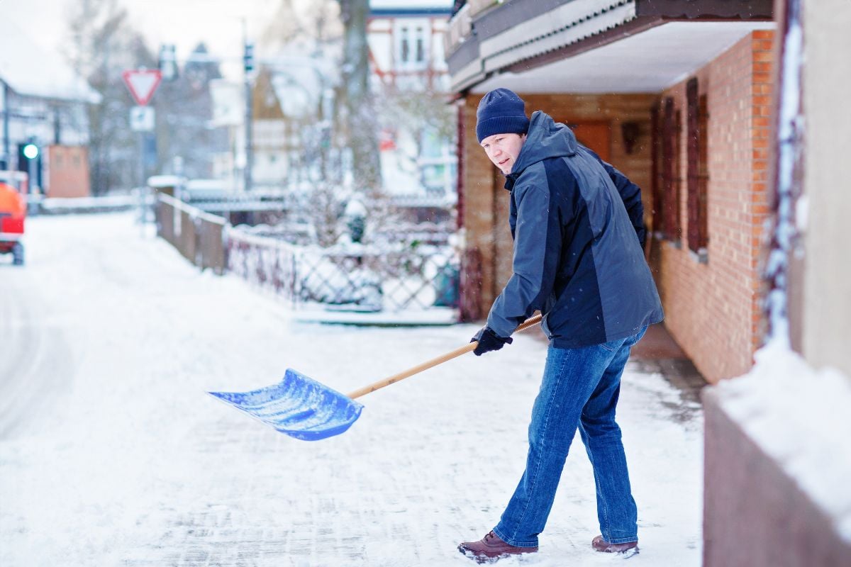 Man with snow shovel cleans sidewalks in winter.