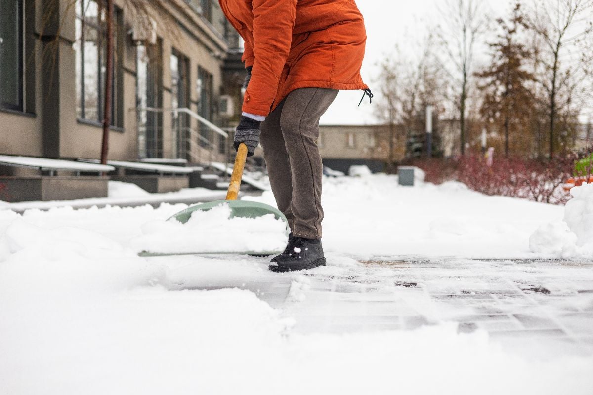 Close-up of a man cleaning and clearing snow in front of the house on a sunny and frosty day.