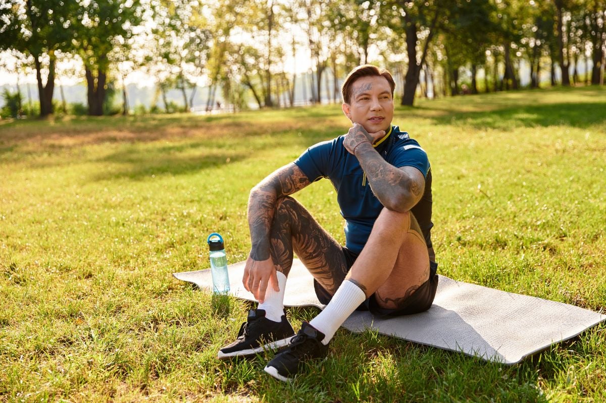 Man sits on a mat, taking a breather during his leisurely walk in the park.