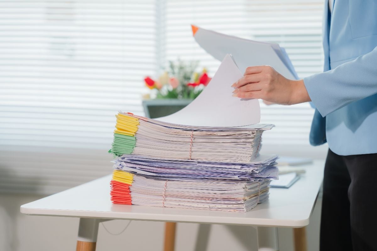 Woman handling stack of paperwork on desk.