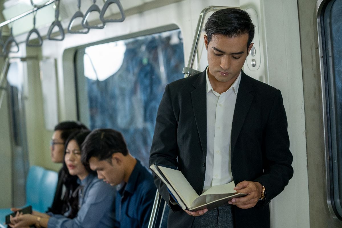 Passenger reading a book while standing on a subway car.