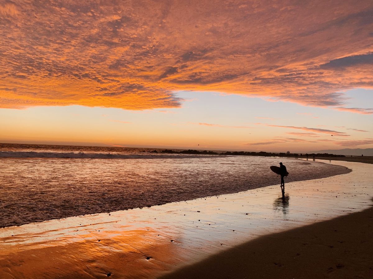 Venice beach California sunrise with surfer by coast horizon.