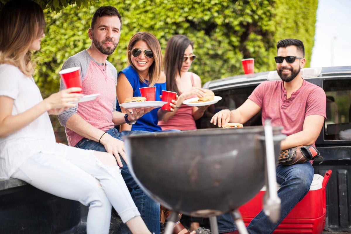 People eating hamburgers next to a grill.