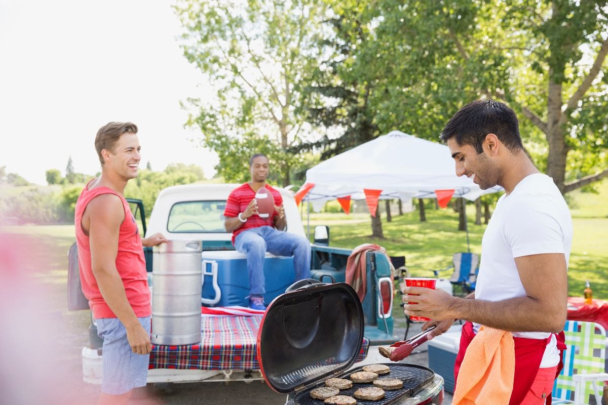 Men relaxing at tailgate barbecue in field.