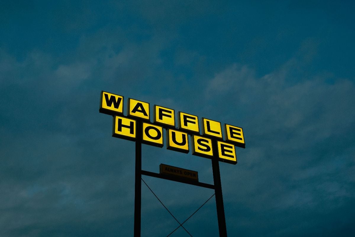 Waffle House sign against a cloudy dark sky.