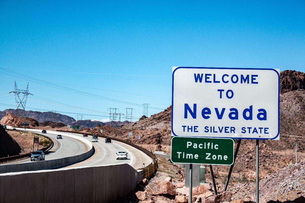 Nevada state welcome sign near highway with desert backdrop.
