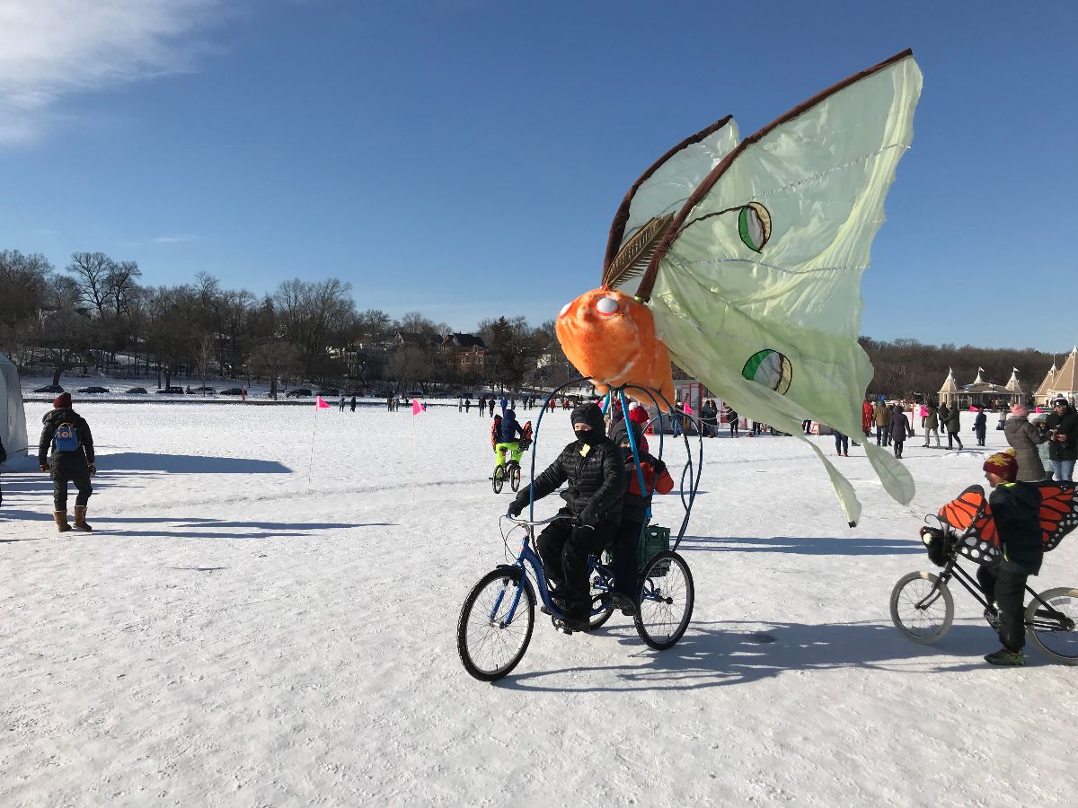A mother and child ride a butterfly bike on a frozen lake art festival.