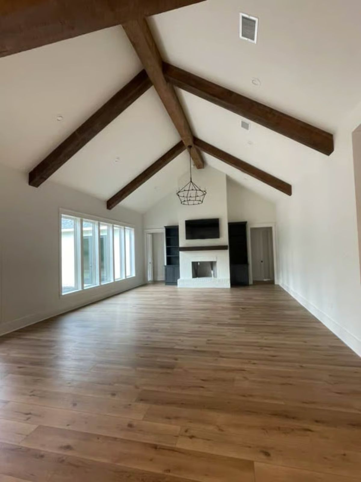 Vaulted Great Room with Exposed Dark Wood Beams and White Fireplace