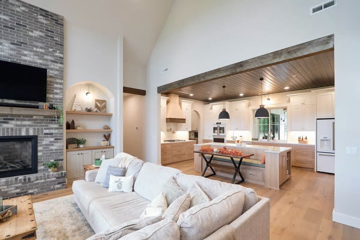 Comfortable Sectional Sofa Facing Gray Brick Fireplace and Wood Beam Kitchen