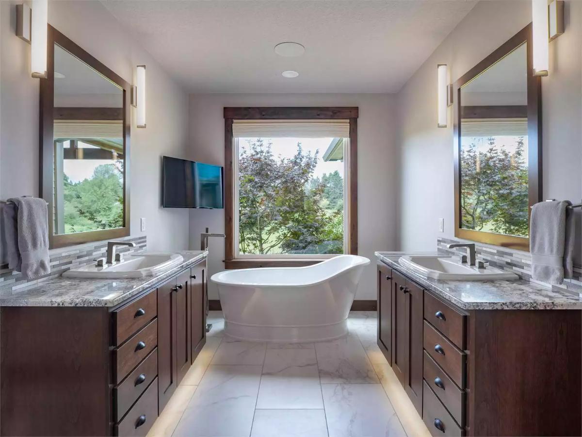 Freestanding Soaking Tub Floats Between Dual Vanities Framed by Dark Wood