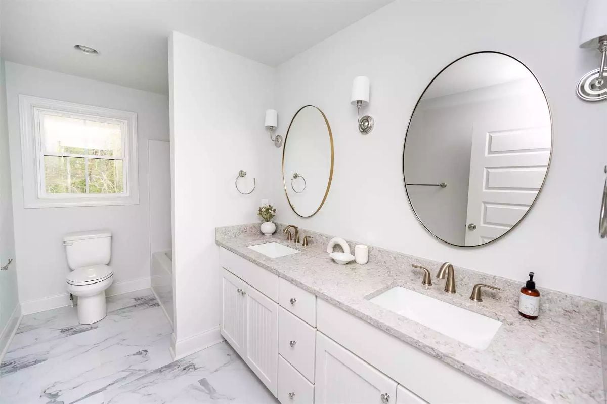 Oval Mirrors and Marble Floors Give a Double Vanity Bathroom Its Character