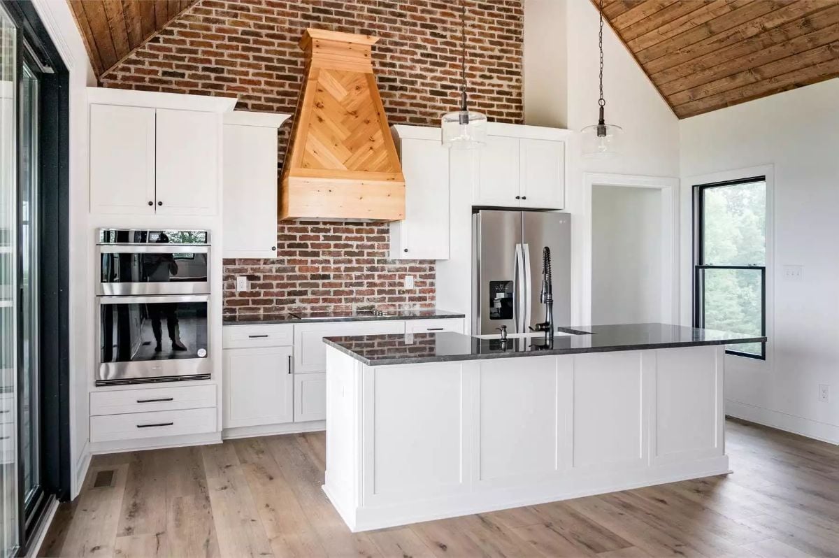 Herringbone Wood Range Hood Anchors a White Kitchen with Exposed Brick