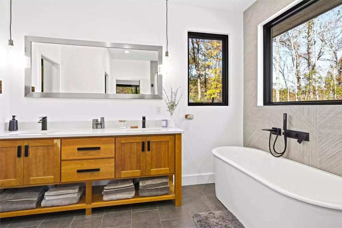 Freestanding Soaking Tub Sits Beneath Black-Framed Windows in Forest-Facing Bath